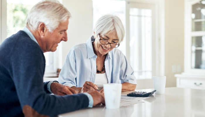 elderly couple filling out forms and using a calculator and smiling for some reason